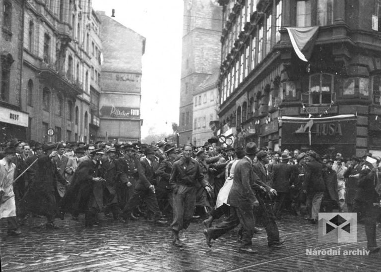 Na rohu Lazarské a Vodičkovy ulice se valí dav českých civilistů a mužů v různých uniformách směrem k budově soudu. Jsou vyzbrojeni noži, šavlemi, revolvery, puškami, dýkami. (Foto: Václav Chochola, archiv autora)